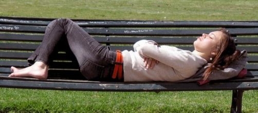 Persona durmiendo en el banco de la plaza.