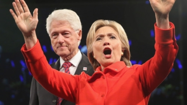 Hilary Clinton vestita di rosso con alle spalle il marito Bill, al primo dibattito con Trump