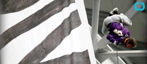 A protestor hanging by a thread over football fans. YouTube (Screencap-Wochit News)