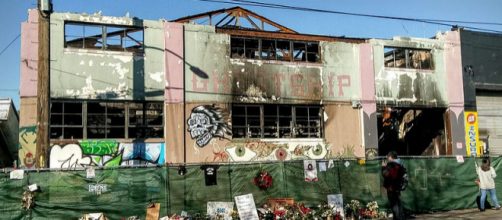 Unidentified observers pass the burned out Ghost Ship live/work warehouse in 2016, a few weeks after fire killed 36.