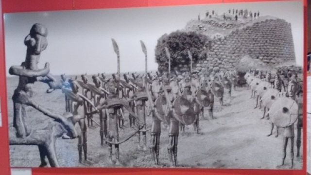 Foto della mostra Omphalos raffigurante un nuraghe e un esercito di bronzetti nuragici.