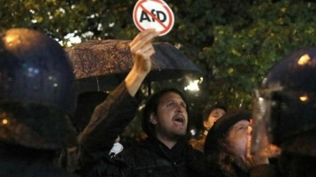 Manifestante antifascista davanti al cordone di polizia con un cartello anti-AfD