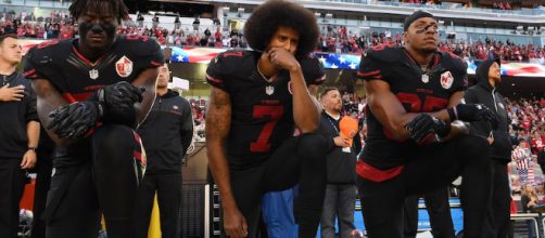 Kaepernick, en el medio, reticente a levantarse durante el himno