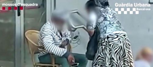 La mujer perteneciente al clan cachea a uno de los hombres forzados a pedir limosna (@Mossos)