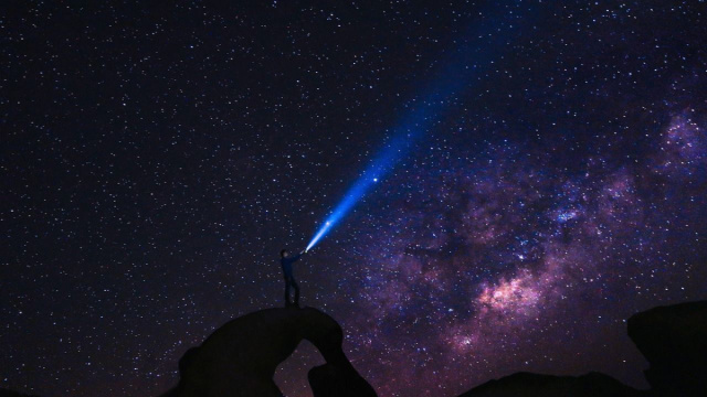 Un uomo con torcia che osserva un cielo stellato &copy; Pixabay