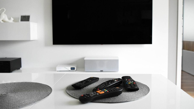 Salotto moderno con tv a parete e quattro telecomandi sul tavolo &copy; Pixabay.