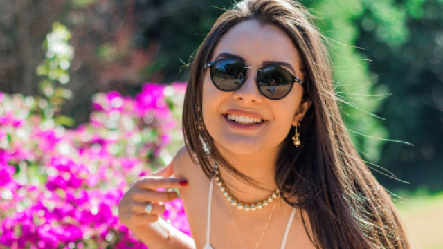 Ragazza con occhiali da sole sorride tra i fiori - &copy; Pixabay.