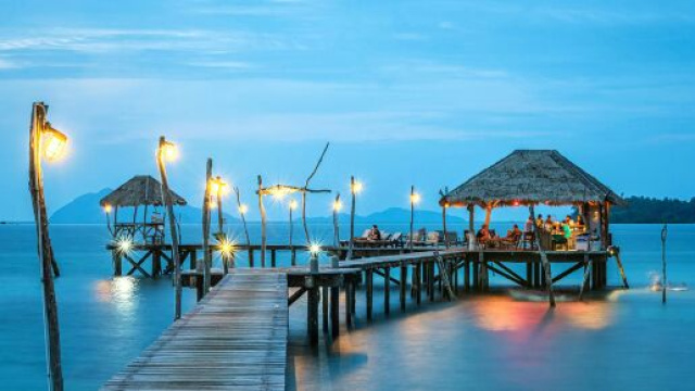 Pontile in legno e capanne illuminate sull&rsquo;acqua al tramonto &ndash; &copy; Pexels.