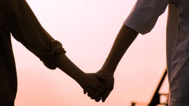 Una coppia che si tiene per mano su un ponte al tramonto &copy; Pixabay.