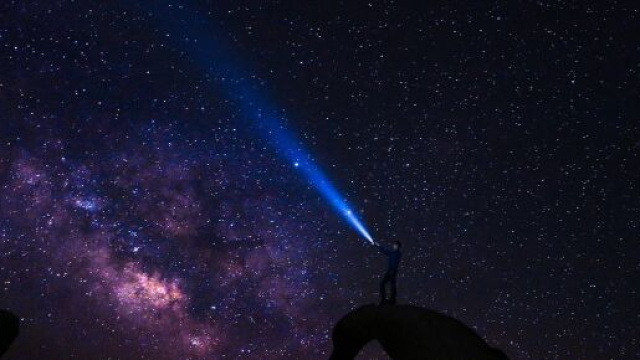 Uomo con pila accesa rivolta al cielo stellato &copy; Pixabay.