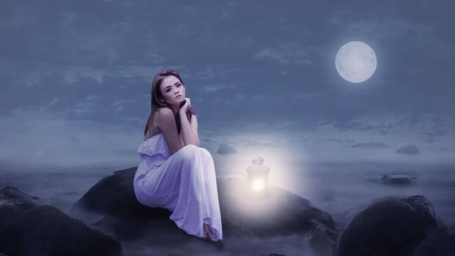 Una donna seduta su uno scoglio con la luna alle spalle - pixabay.com