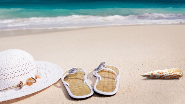infradito, capello e conchiglia sulla spiaggia &copy; Pixabay.